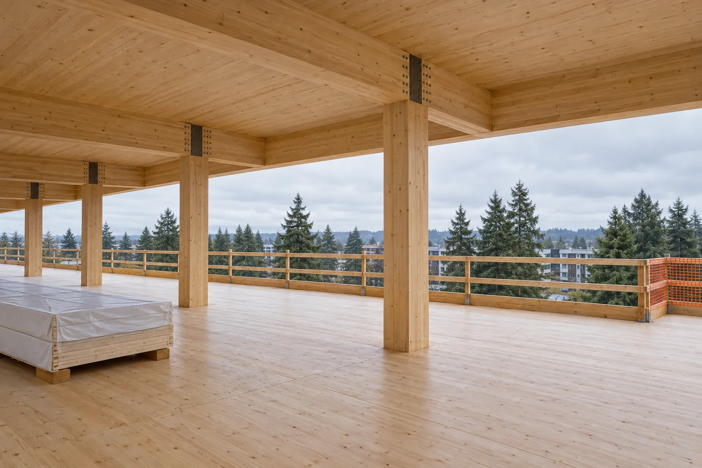 Open mass timber floor with glulam columns and beams, a CLT deck and ceiling, a wrapped panel stack on blocking, and a continuous perimeter guardrail